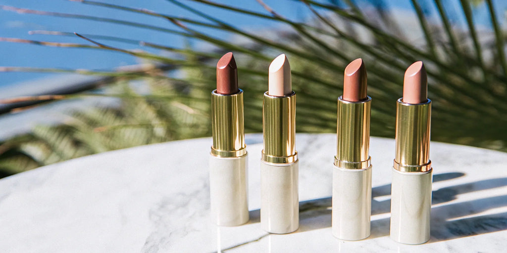 A collection of hydrating nude lipsticks in gold tubes arranged on a marble surface.
