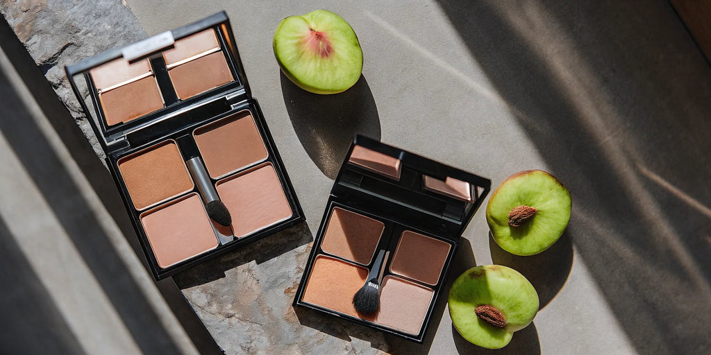 A flat lay of peachy blush palettes, makeup brushes, and fresh peach slices.